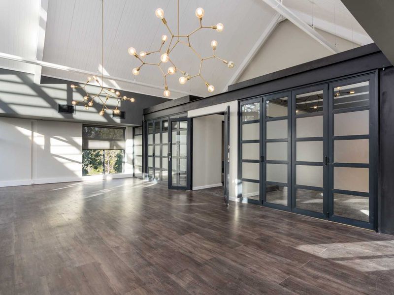Spacious modern office area featuring high vaulted ceilings, exposed beams, contemporary glass partitions, and high-quality laminate flooring with abundant natural light.