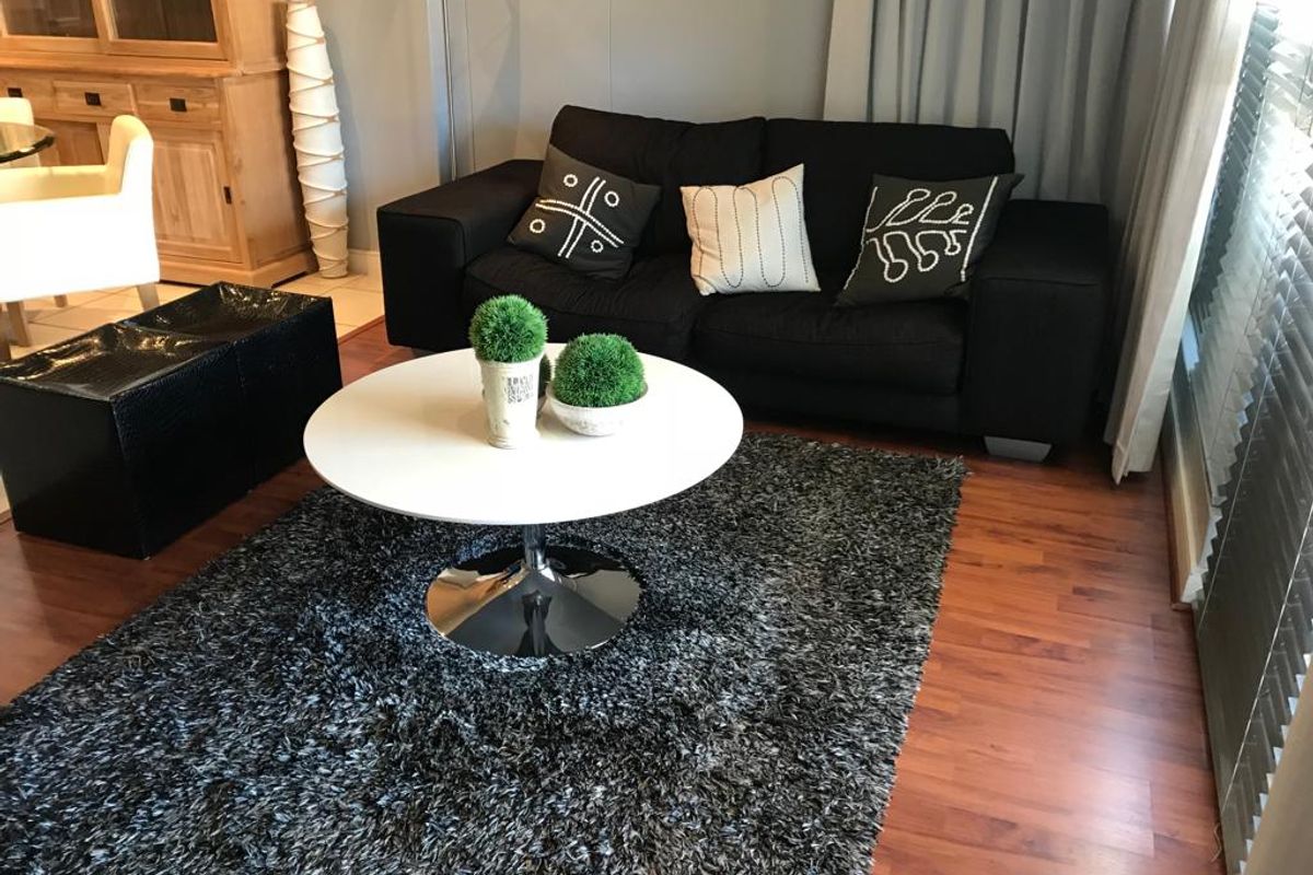 A living room area featuring warm-toned laminate wood flooring and large windows with fitted blinds, providing a comfortable and functional space.