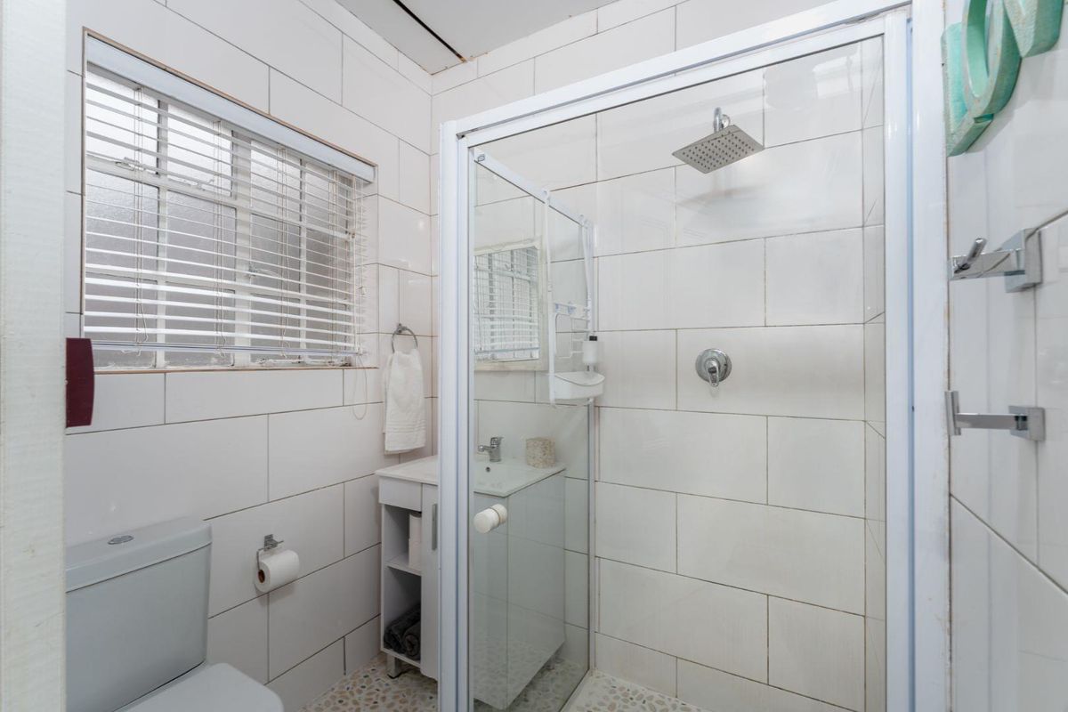 Compact bathroom featuring a glass-enclosed shower with a rain shower head, a vanity basin, and a toilet, finished with white wall tiles.
