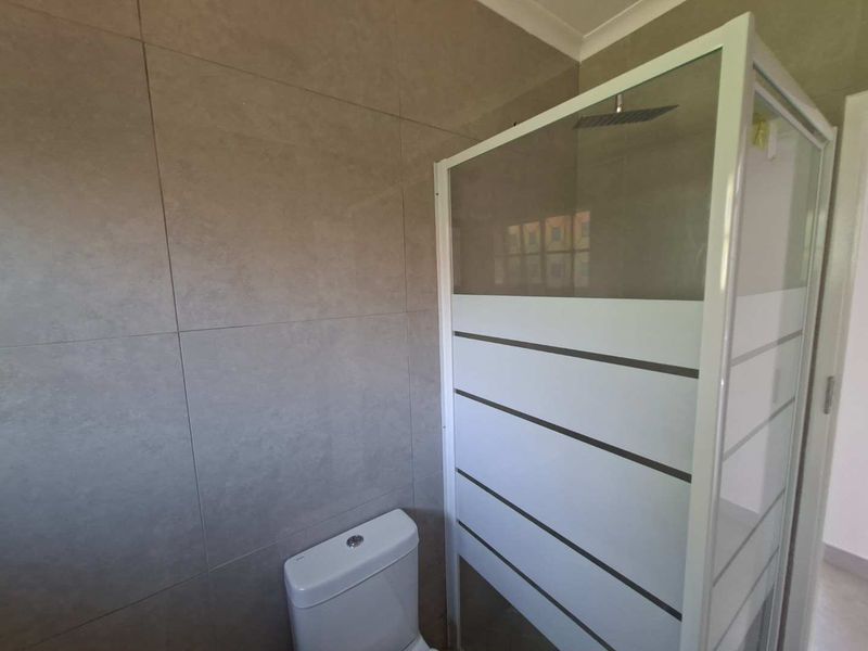 A clean, modern bathroom featuring a glass-enclosed shower with a rain shower head and a white toilet against neutral tiled walls.