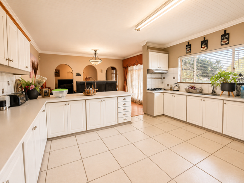Spacious kitchen featuring white cabinetry, laminate countertops, gas cooktop, and tiled flooring, with an open-plan layout connecting to the adjacent living area.