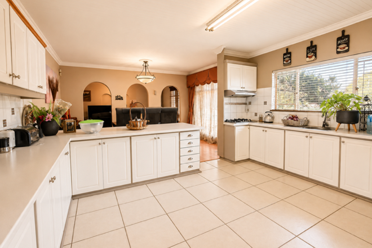 Spacious kitchen featuring white cabinetry, laminate countertops, gas cooktop, and tiled flooring, with an open-plan layout connecting to the adjacent living area.
