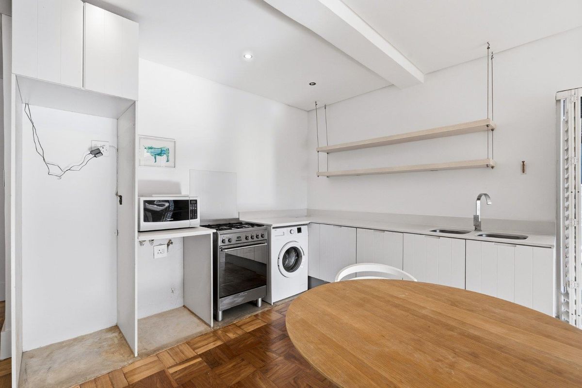 Compact kitchen featuring white cabinetry, integrated sink, built-in shelving, and space for a stove and washing machine, set against classic parquet flooring.