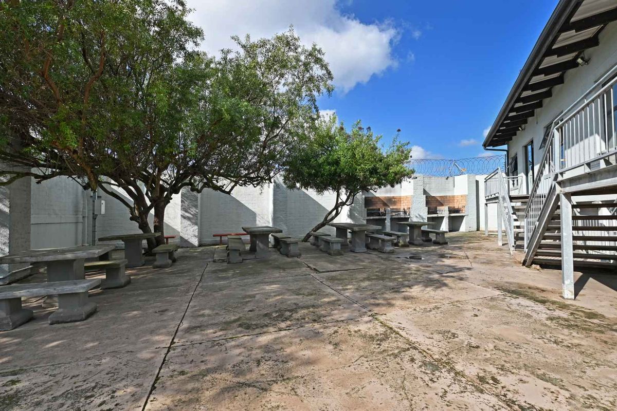 Outdoor communal courtyard area featuring concrete paving, built-in brick braai facilities, and established trees, adjacent to the apartment building exterior.