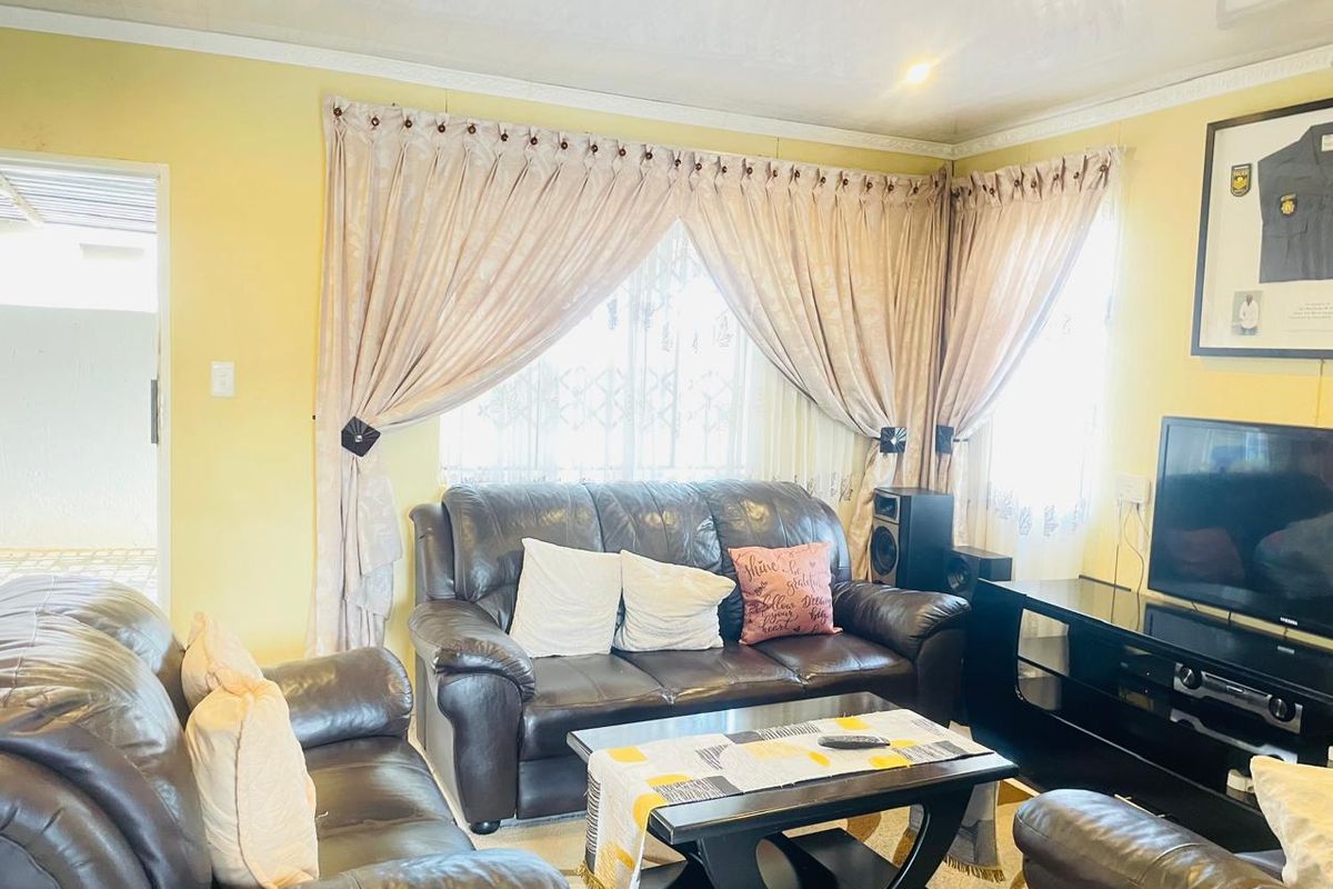 A comfortable living room featuring yellow walls, crown molding, and large windows with decorative curtains, providing a bright and inviting space.