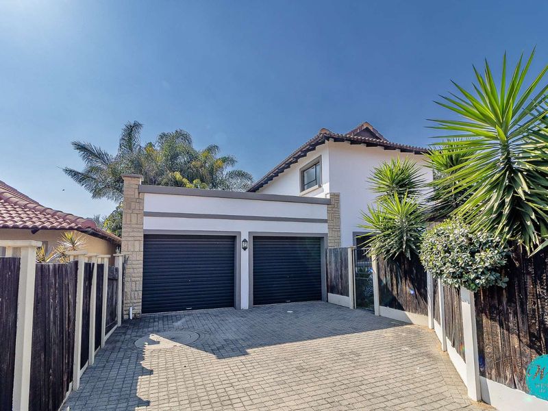 Front view of the property featuring a double garage with roller shutter doors and a paved driveway, enclosed by timber fencing.