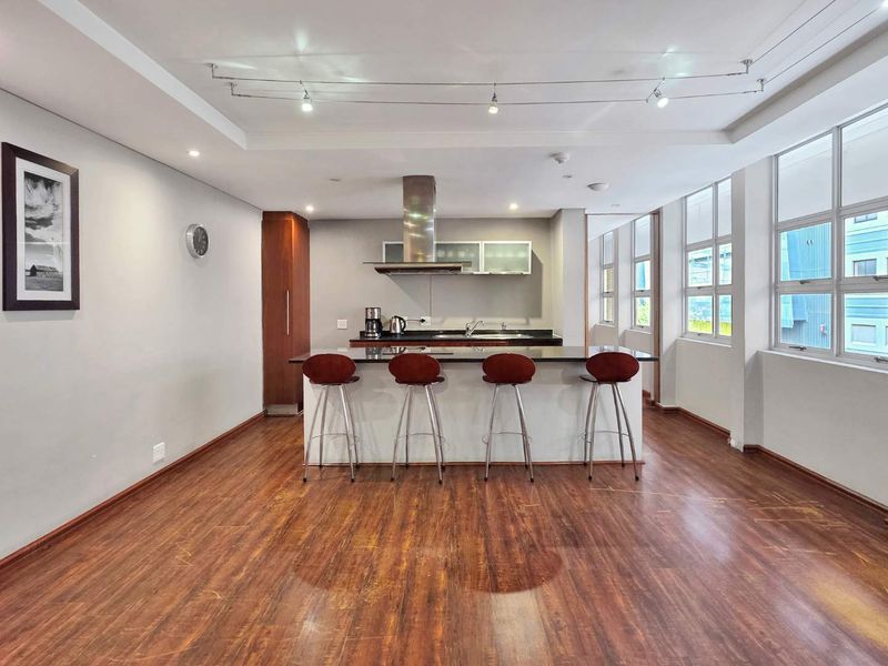 Open-plan living and kitchen area featuring a central island, modern extractor fan, laminate flooring, and large windows providing ample natural light.