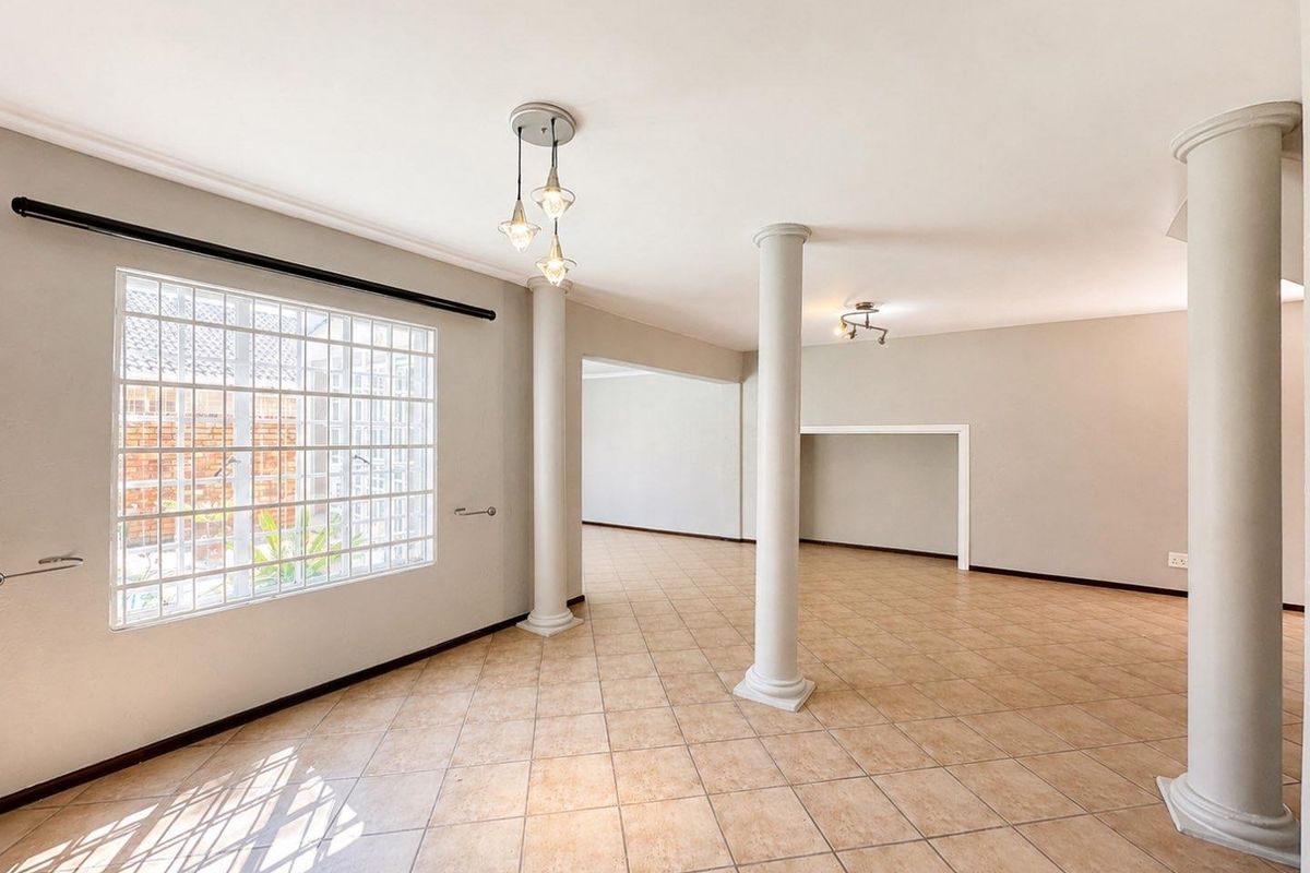 Spacious open-plan living area featuring ceramic tile flooring, decorative columns, and a unique glass block window, offering a bright and versatile layout.