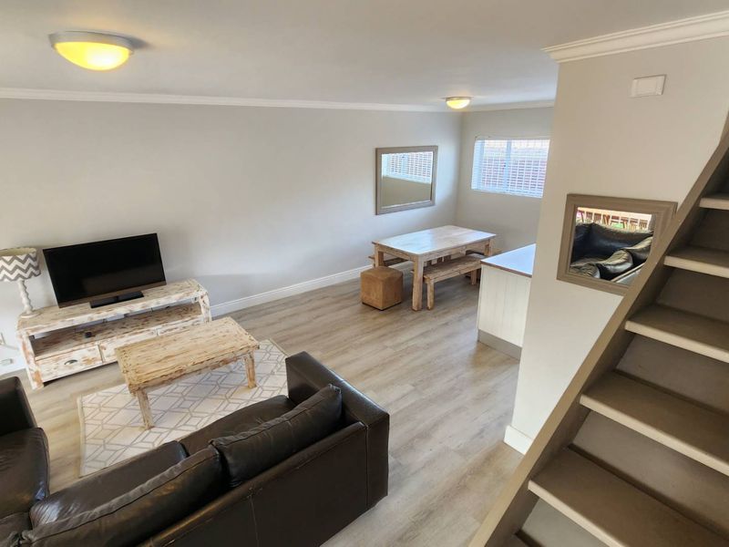 Open plan living and dining area featuring light-toned laminate flooring, neutral walls, and a staircase leading to the upper level.