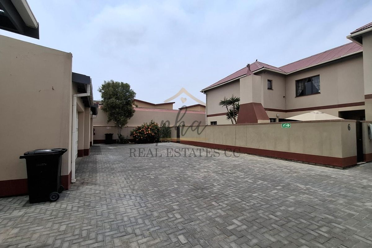 A paved communal driveway and courtyard area within an apartment complex, featuring perimeter walls and access to residential units.