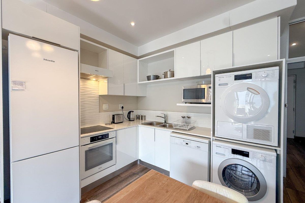 Modern compact kitchen featuring high-gloss white cabinetry, integrated Miele appliances, built-in oven, hob, extractor fan, and a double sink with tiled splashback.