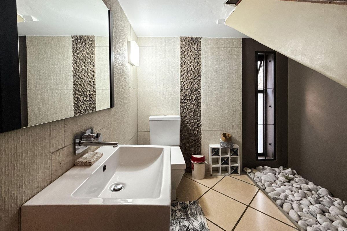Modern bathroom featuring a wall-mounted basin, toilet, decorative stone wall accents, and a unique pebble floor feature under the staircase.