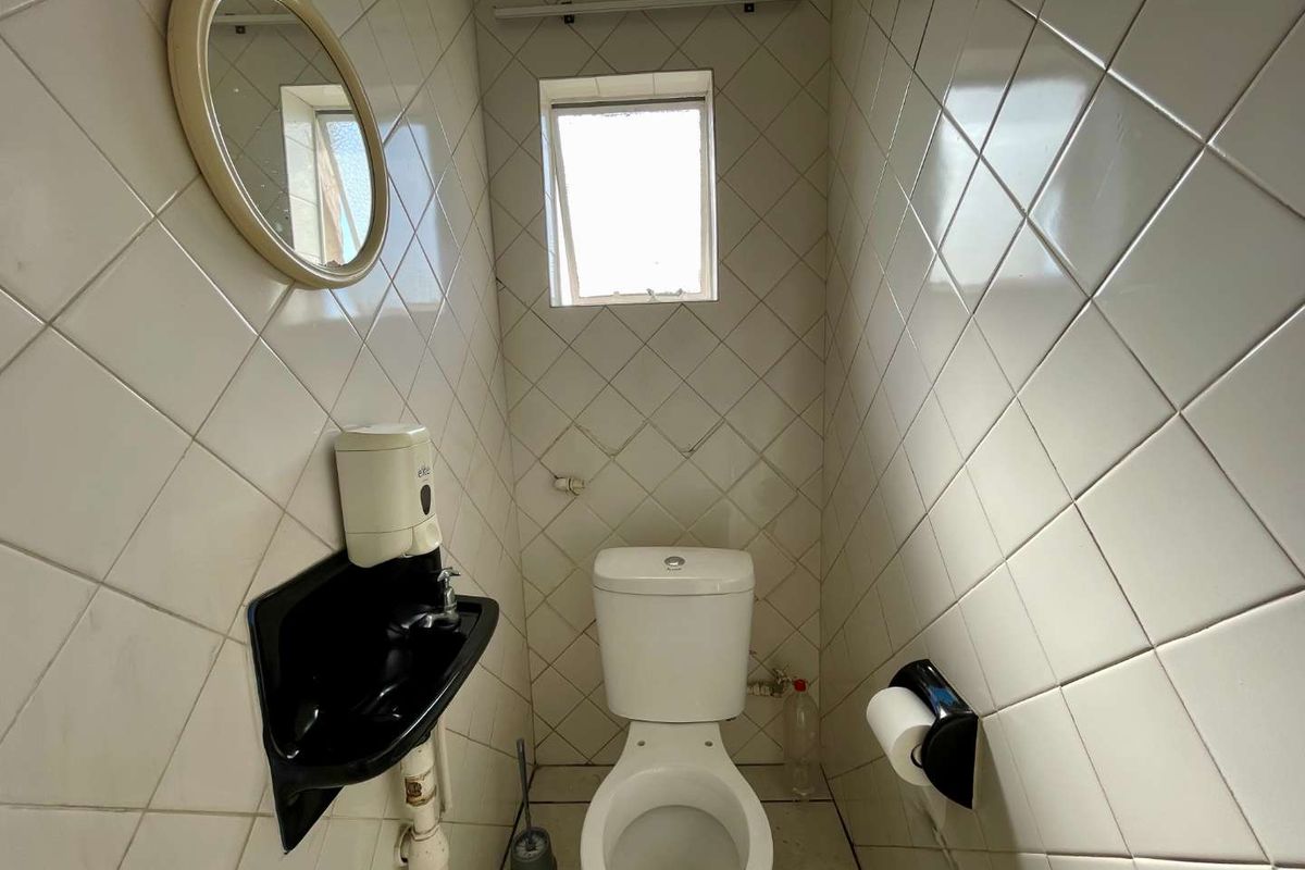 A compact guest bathroom featuring a wall-mounted basin, toilet, and fully tiled walls with a small window for ventilation.