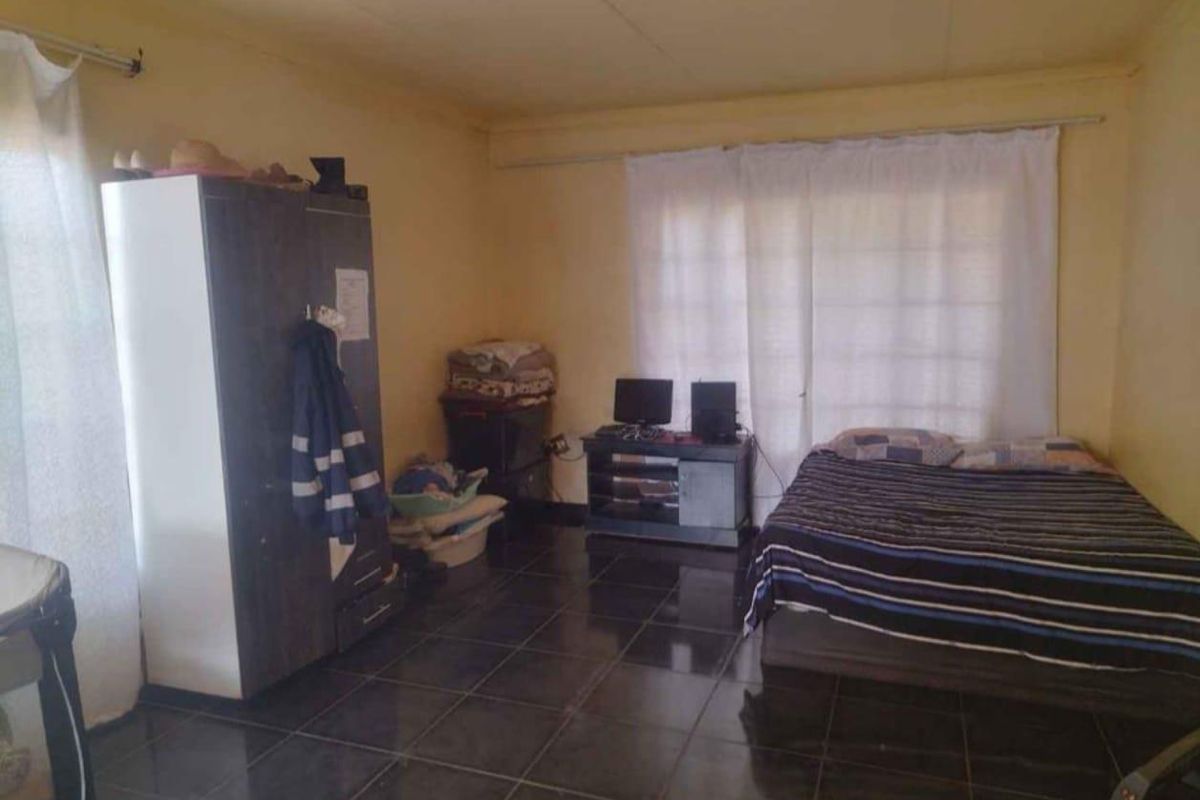 A bedroom featuring dark tiled flooring and a sliding door, currently showing signs of wear on the ceiling and walls.