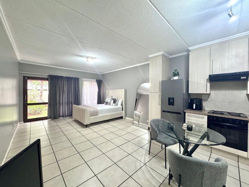 Open-plan studio apartment featuring tiled flooring, a functional kitchen with built-in appliances, and direct access to an outdoor area via a sliding door.