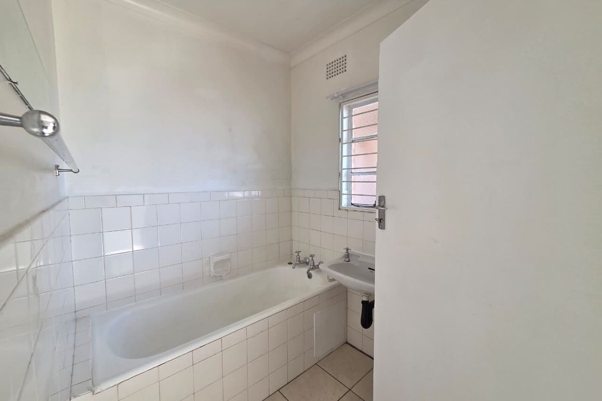 A functional, dated bathroom featuring a built-in bathtub, wall-mounted basin, and tiled finishes, offering a blank canvas for renovation.