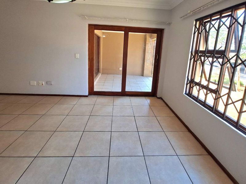 An empty living room featuring tiled flooring, a sliding door leading to a patio, and windows fitted with security bars.