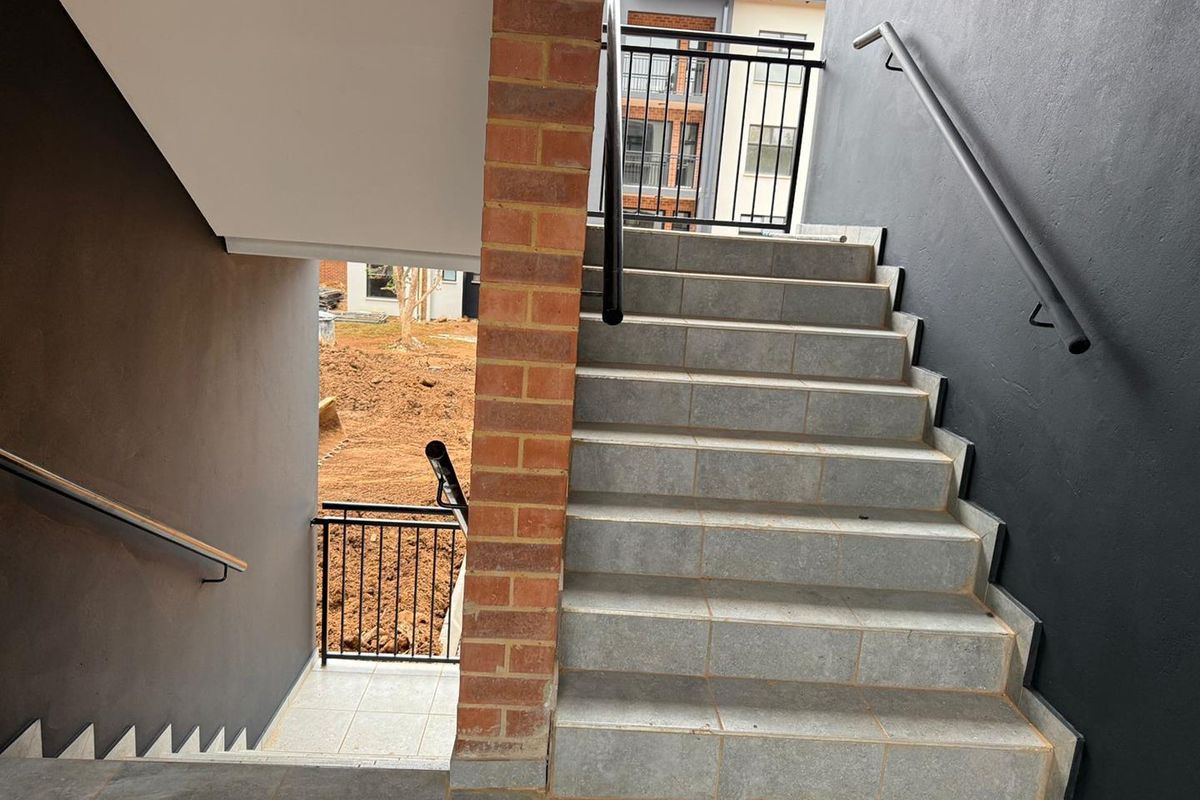 External staircase featuring tiled steps, brick pillar support, and modern black metal handrails leading to an apartment entrance.