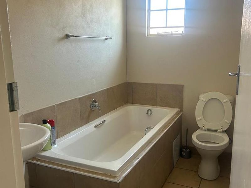 A functional bathroom featuring a built-in bathtub with tiled surround, pedestal sink, and toilet, finished with ceramic floor tiles.