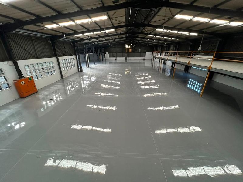 Spacious industrial warehouse featuring a polished epoxy floor, high ceilings with skylights, and an integrated mezzanine level for additional storage or office space.