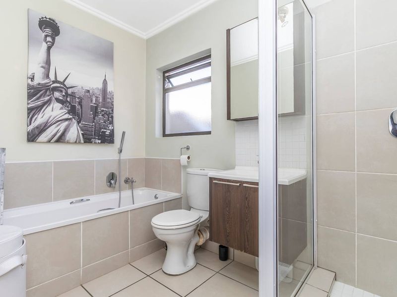 A well-maintained bathroom featuring a built-in bathtub, separate shower enclosure, vanity cabinet, and neutral wall and floor tiling.