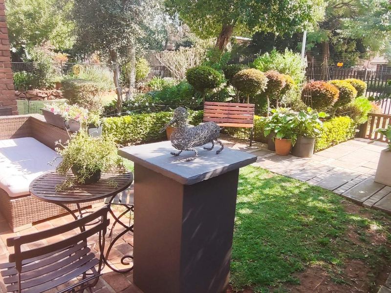 A charming outdoor patio area featuring brick paving, an exposed brick wall, and a well-maintained landscaped garden.