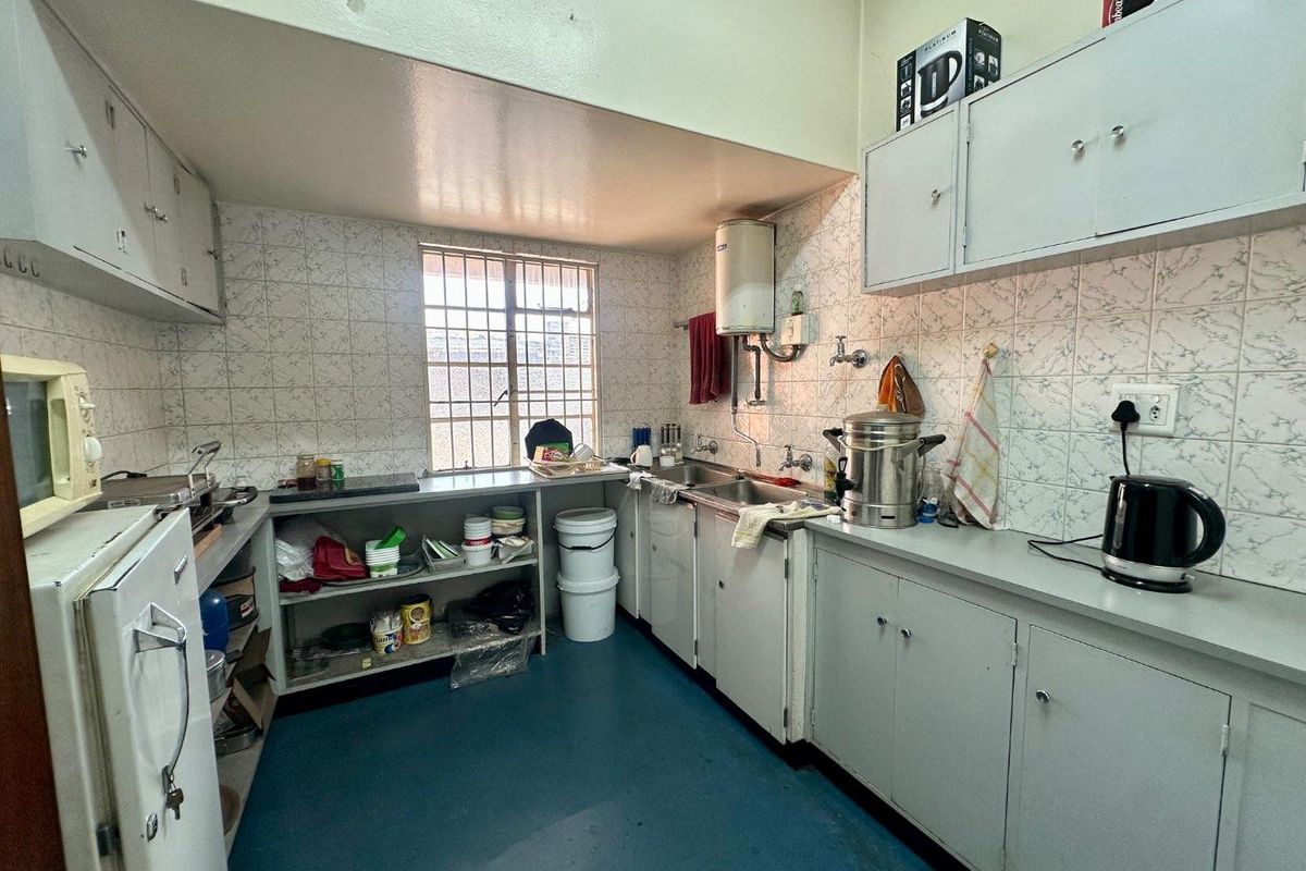 A functional industrial kitchen featuring built-in cabinetry, tiled splashbacks, a stainless steel sink, and a wall-mounted geyser unit.