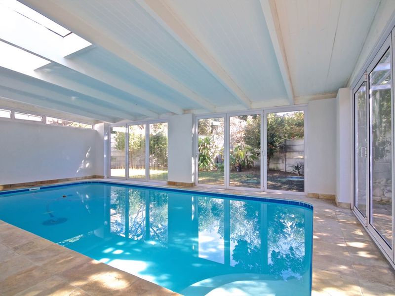 Bright indoor swimming pool area featuring a large skylight, exposed beam ceiling, and expansive sliding glass doors opening to the garden.