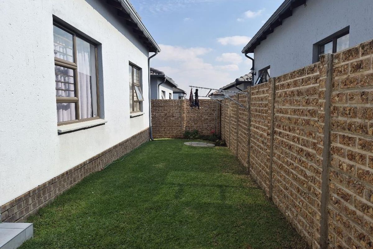 A side garden area featuring a manicured lawn, enclosed by a textured brick boundary wall and the exterior wall of the townhouse.