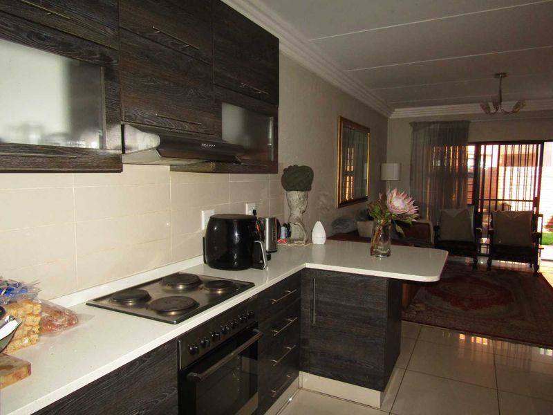 Open-plan kitchen featuring dark wood cabinetry, built-in oven, electric hob, and a breakfast bar, flowing into the adjacent living area.
