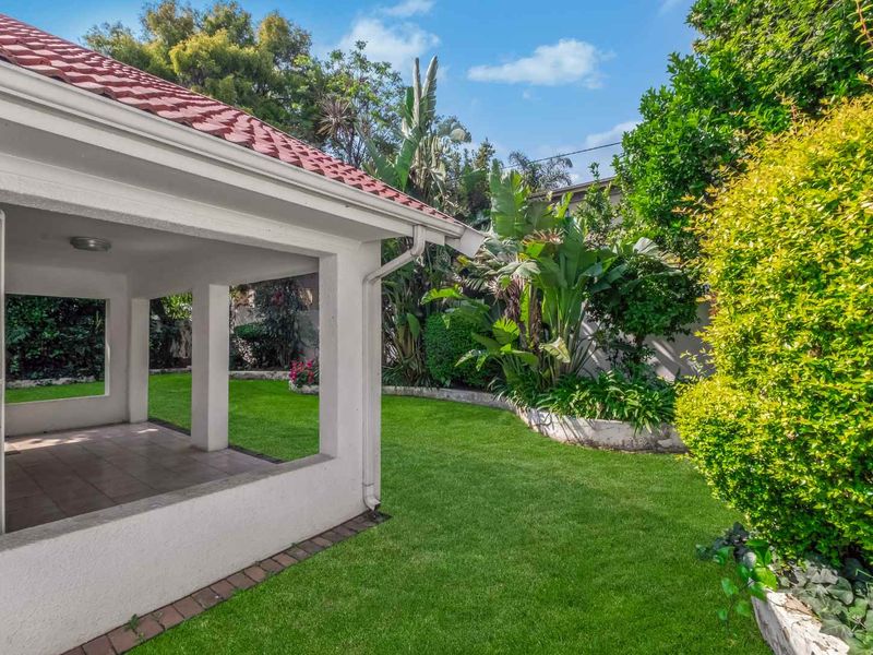 A covered patio area overlooking a well-maintained private garden with lush greenery and a lawn.