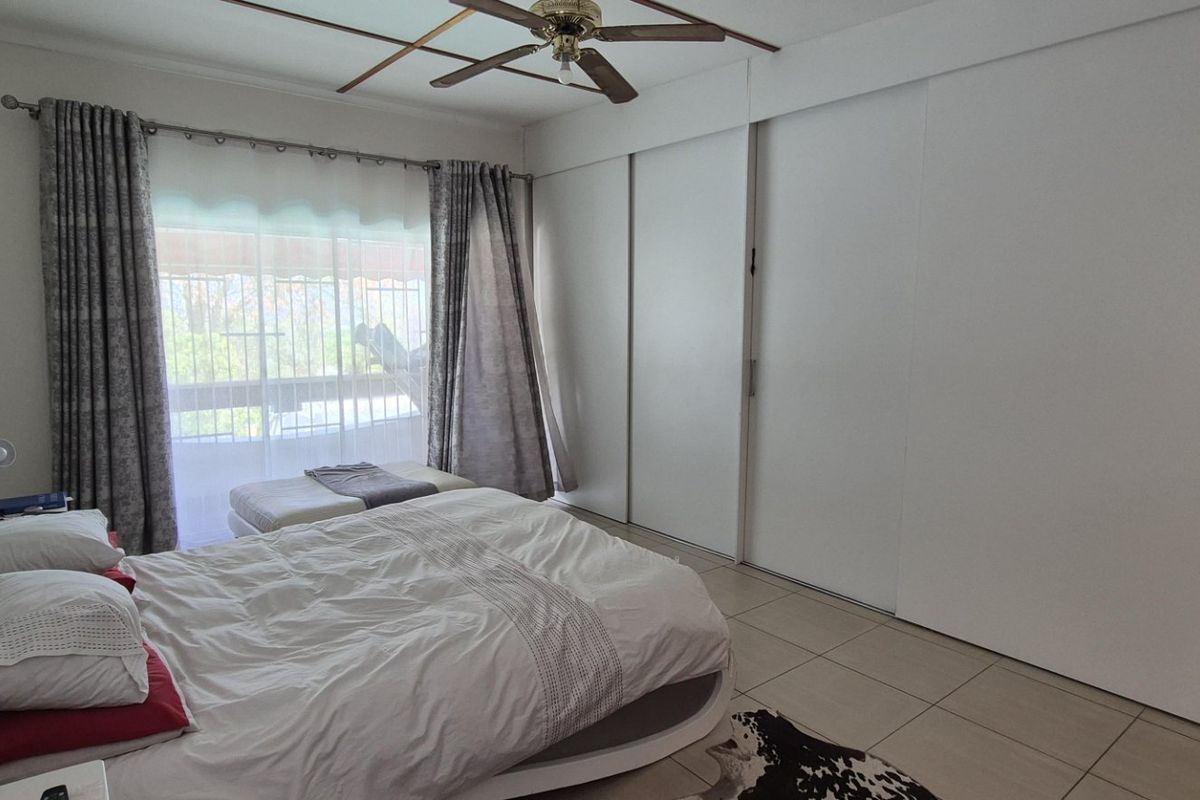 A bedroom featuring tiled flooring, built-in sliding door wardrobes, and a ceiling fan, with access to an outdoor area via a sliding glass door.