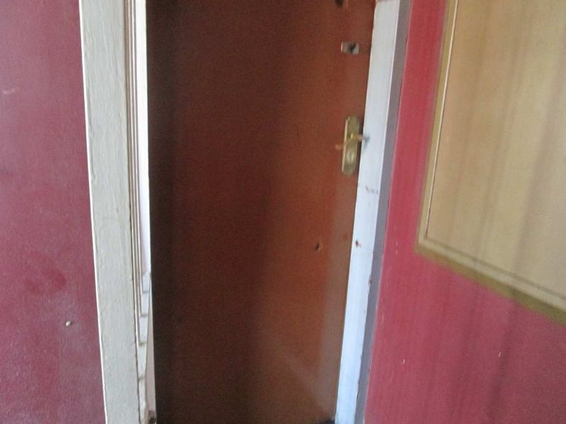 A close-up view of an apartment entrance door showing signs of wear on the surrounding door frame and wall surfaces.