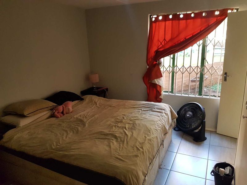 A standard bedroom featuring tiled flooring and a window fitted with a security gate, providing natural light and ventilation.