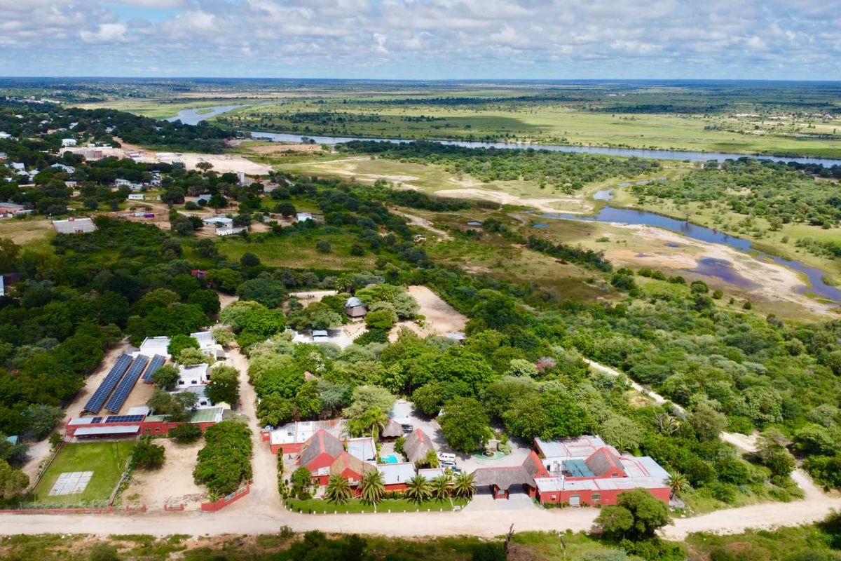 Aerial view of a lodge property featuring multiple buildings, thatched roofs, a swimming pool, and extensive solar panel installations set within a natural landscape.