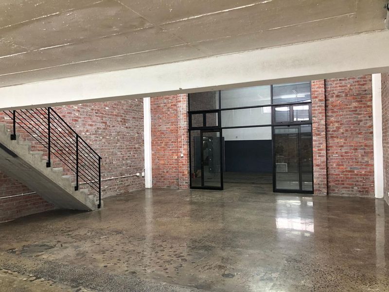 Spacious open-plan industrial style area featuring exposed brick walls, polished concrete floors, and a concrete staircase with a modern metal balustrade.