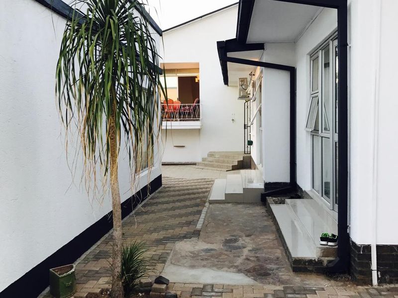 A paved exterior walkway between guest house buildings featuring modern white facades with black trim and aluminium window frames.