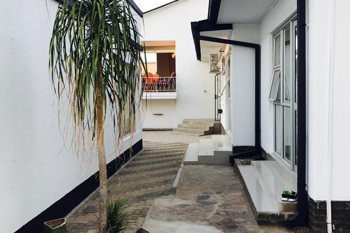 A paved exterior walkway between guest house buildings featuring modern white facades with black trim and aluminium window frames.