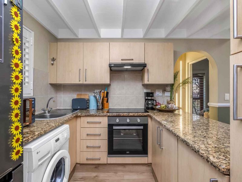 Compact kitchen featuring light wood cabinetry, granite countertops, built-in oven, electric hob, and an integrated laundry space, finished with an exposed beam ceiling.