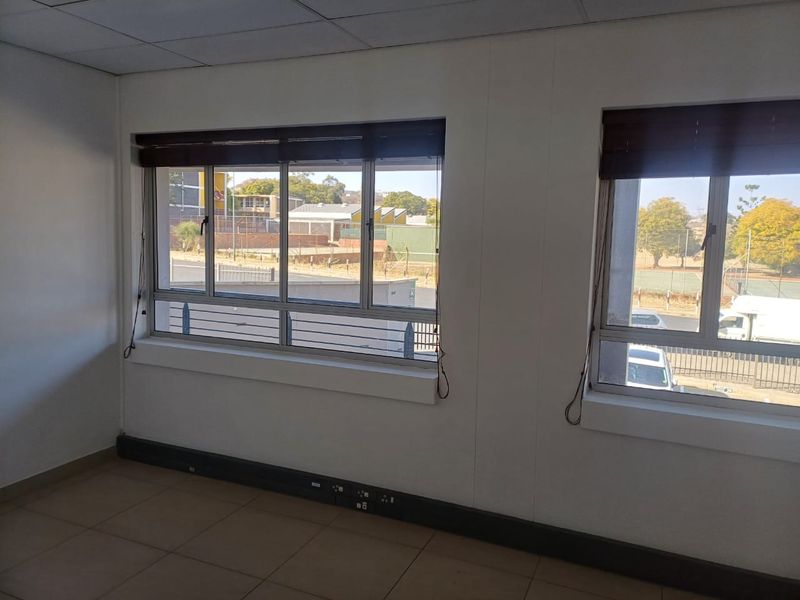 A bright, empty office space featuring tiled flooring, suspended ceilings, and large windows with fitted blinds, offering a functional workspace environment.