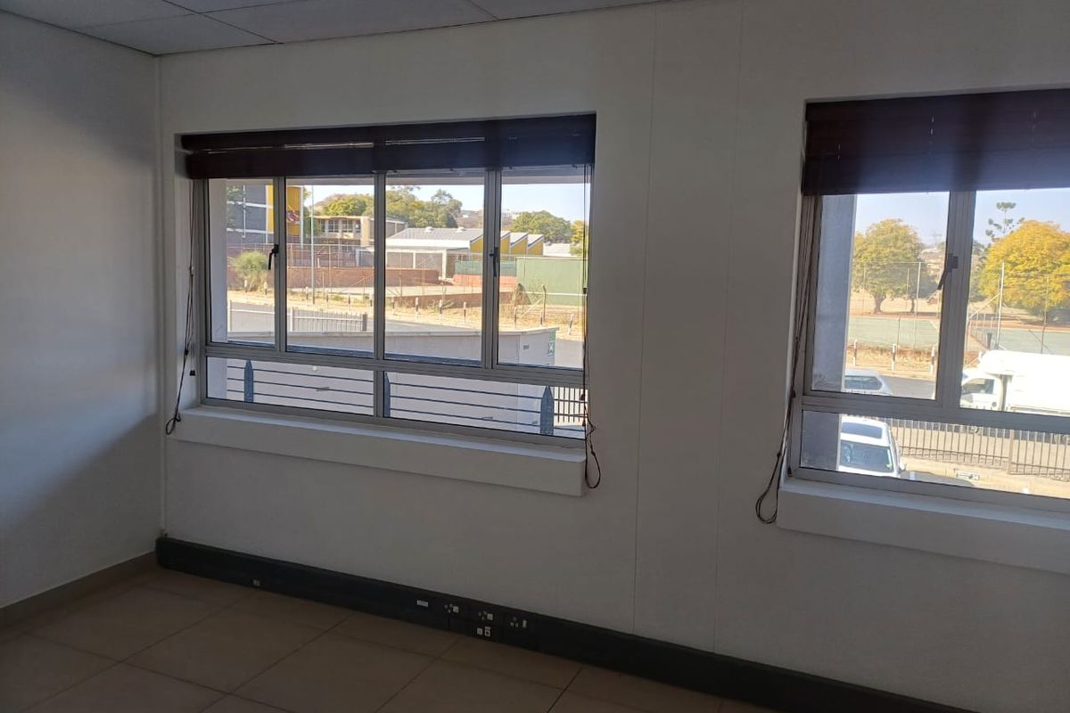 A bright, empty office space featuring tiled flooring, suspended ceilings, and large windows with fitted blinds, offering a functional workspace environment.