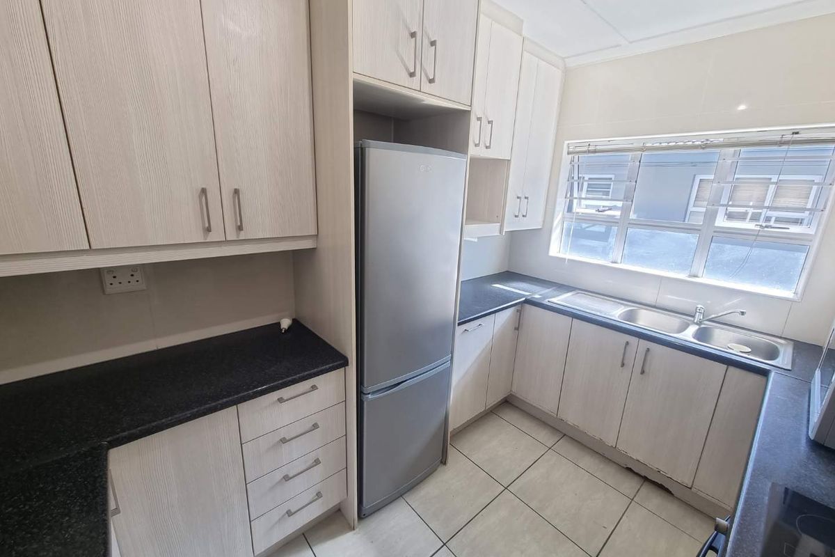 A functional kitchen featuring light-toned laminate cabinetry, dark granite countertops, a double stainless steel sink, and tiled flooring with natural light.