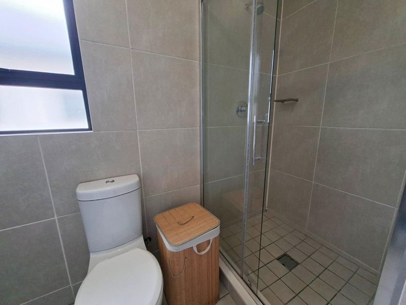A clean, modern bathroom featuring a glass-enclosed shower, tiled walls, and a standard toilet.