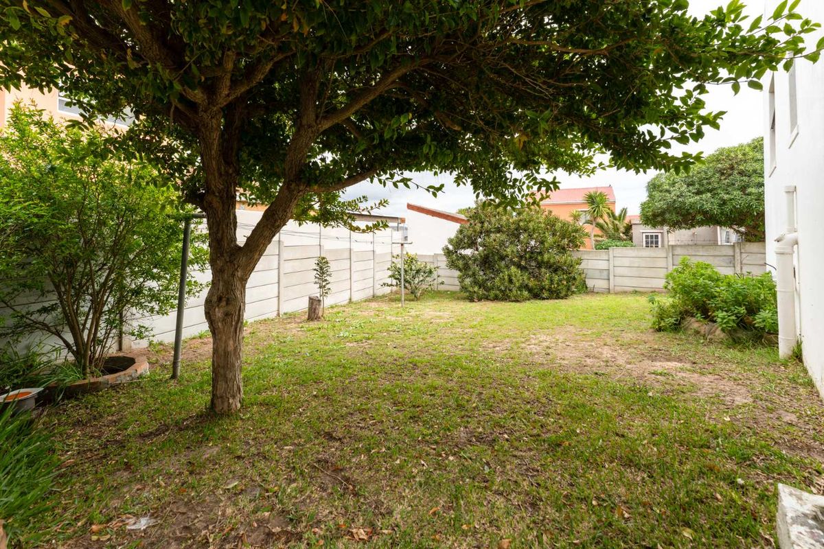 A private rear garden featuring a mature tree, established shrubs, and a concrete boundary wall, offering a blank canvas for landscaping.