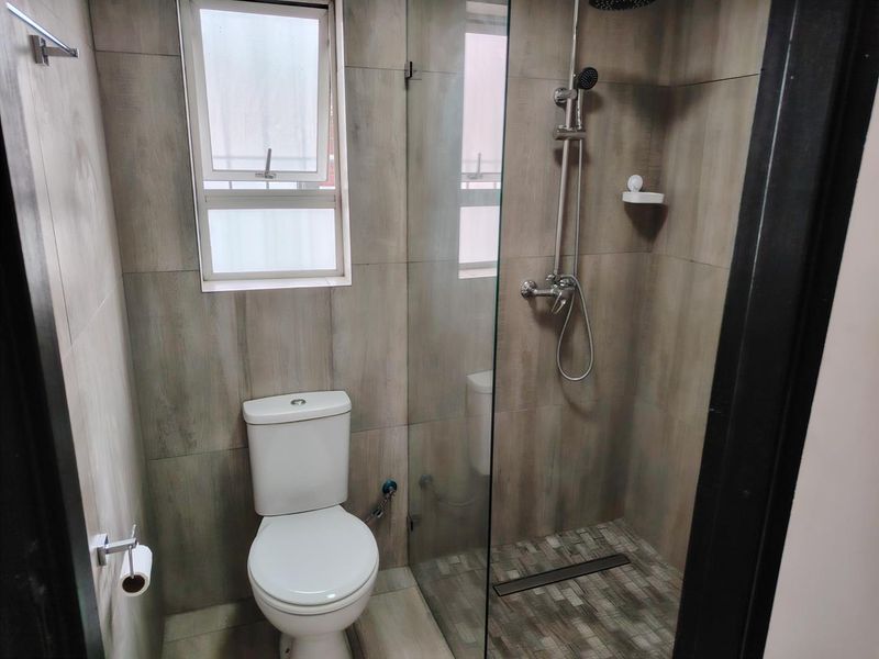 Modern bathroom featuring a walk-in shower with glass screen, tiled finishes, and a standard toilet.
