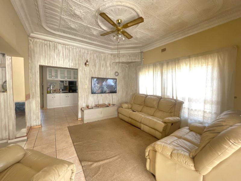 Open plan living area featuring an ornate pressed metal ceiling, ceiling fan, and tiled flooring, with an adjacent kitchen visible.