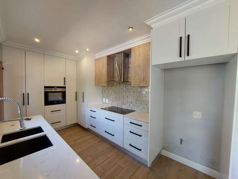 Modern kitchen featuring white and wood-tone cabinetry, quartz countertops, a built-in oven, hob, extractor fan, and a double sink with contemporary finishes.