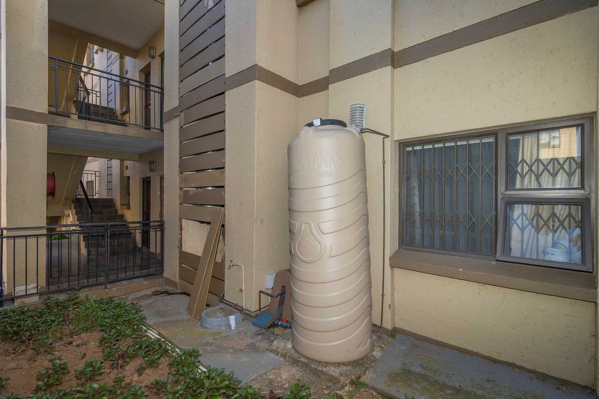 Exterior view of an apartment building common area featuring a large water storage tank, security-barred windows, and stairwell access.