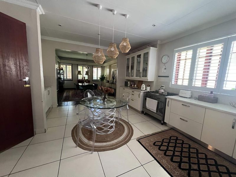 Open-plan kitchen and dining area featuring white cabinetry, gas stove, tiled flooring, and natural light through shutter blinds.
