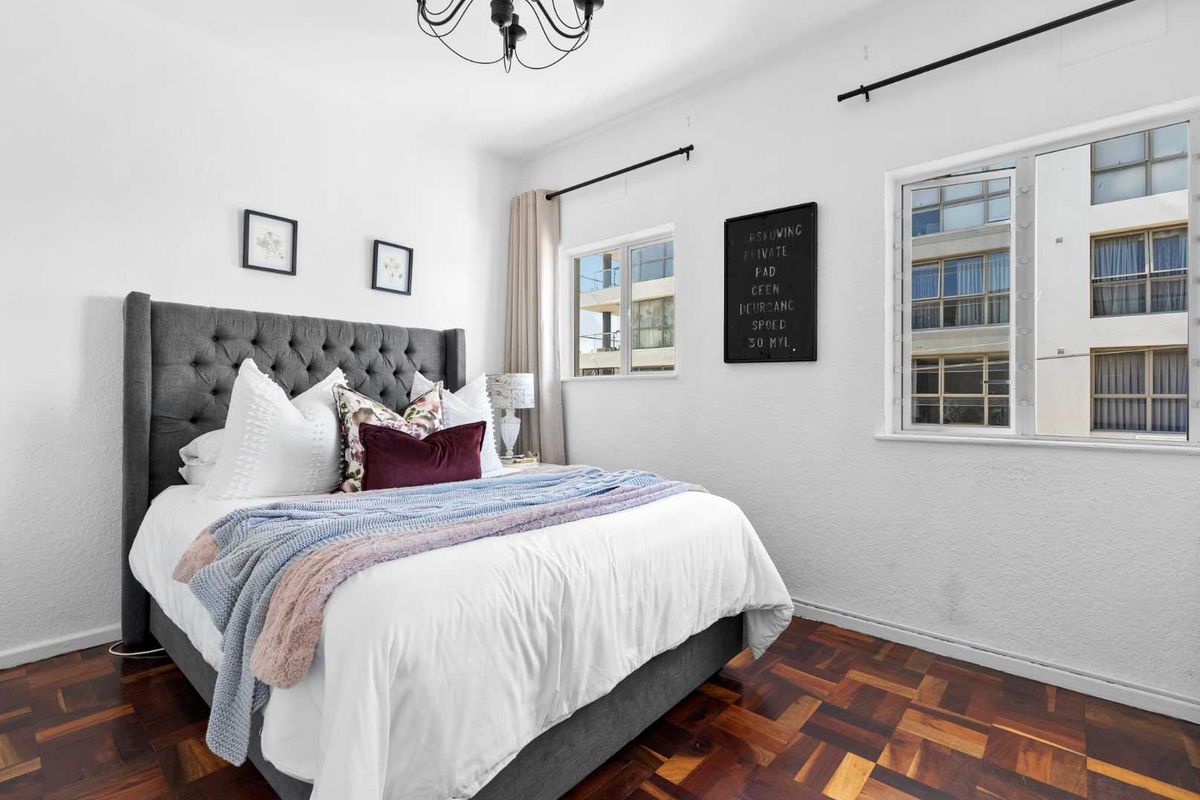 A well-maintained bedroom featuring classic parquet flooring, neutral walls, and large windows that provide ample natural light.